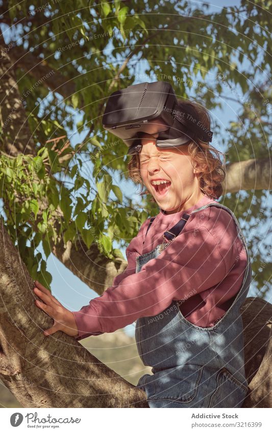 Junge in Virtual-Reality-Brille im Baum sitzend Virtuelle Realität freudig Sitzen Glück Kind wenig heiter Kindheit Spaß Lächeln zuschauend lässig Natur Sommer