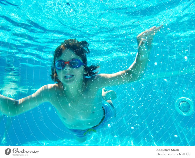 Lustiger Junge schwimmt unter Wasser und schaut in die Kamera schwimmen Pool lustig Grimasse Atem Halt Kind heiter spielerisch Sommer Kindheit Sinkflug