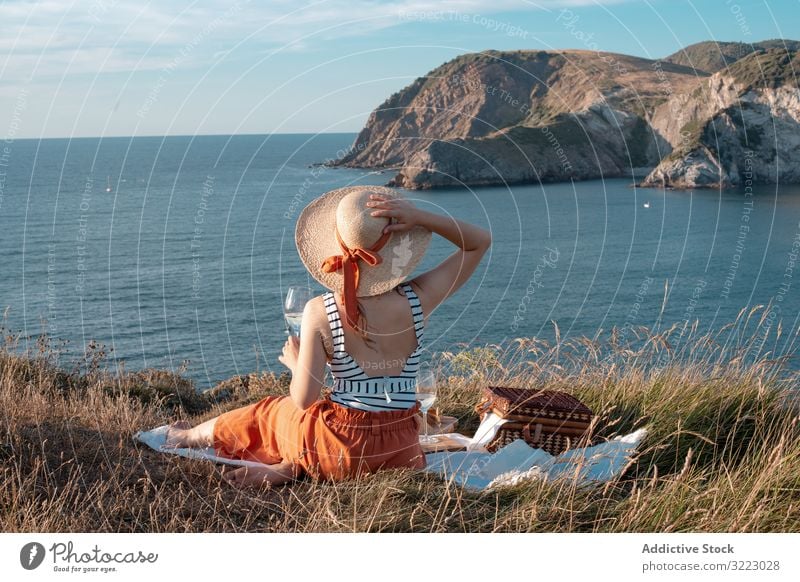 Frau mit Glas Getränk auf Picknickmatte mit Blick auf Meer und Berge Seeküste Strand Sommer lesen Freizeit Himmel MEER sich[Akk] entspannen trinken Urlaub