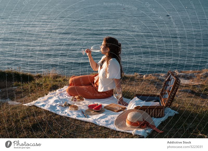 Frau mit Glas Getränk auf Picknickmatte mit Blick auf Meer und Berge Seeküste Strand Sommer lesen Freizeit Himmel MEER sich[Akk] entspannen trinken Urlaub