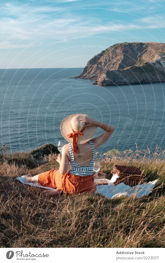 Frau mit Glas Getränk auf Picknickmatte mit Blick auf Meer und Berge Seeküste Strand Sommer lesen Freizeit Himmel MEER sich[Akk] entspannen trinken Urlaub