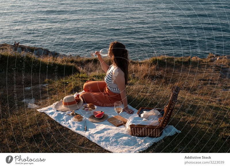 Frau mit Glas Getränk auf Picknickmatte mit Blick auf Meer und Berge Seeküste Strand Sommer lesen Freizeit Himmel MEER sich[Akk] entspannen trinken Urlaub