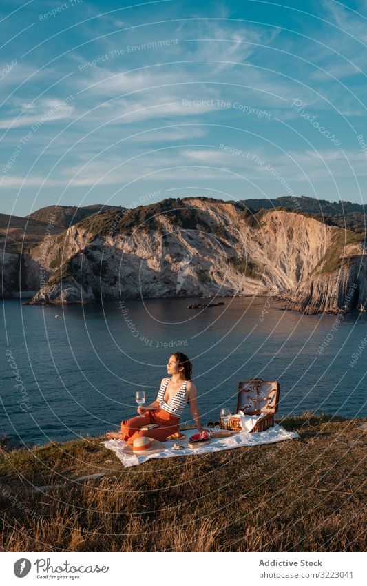 Frau mit Glas Getränk auf Picknickmatte mit Blick auf Meer und Berge Seeküste Strand Sommer lesen Freizeit Himmel MEER sich[Akk] entspannen trinken Urlaub