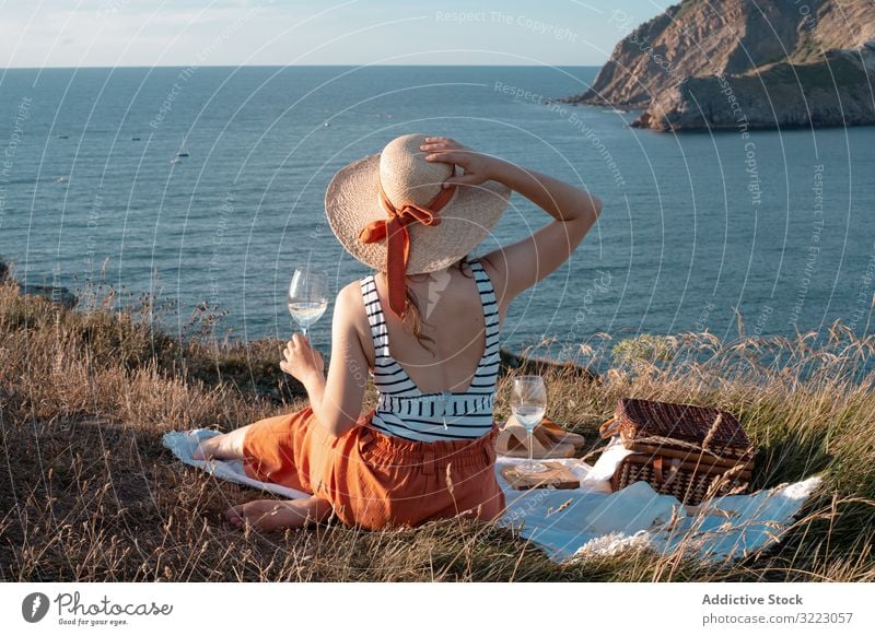 Frau mit Glas Getränk auf Picknickmatte mit Blick auf Meer und Berge Seeküste Strand Sommer lesen Freizeit Himmel MEER sich[Akk] entspannen trinken Urlaub