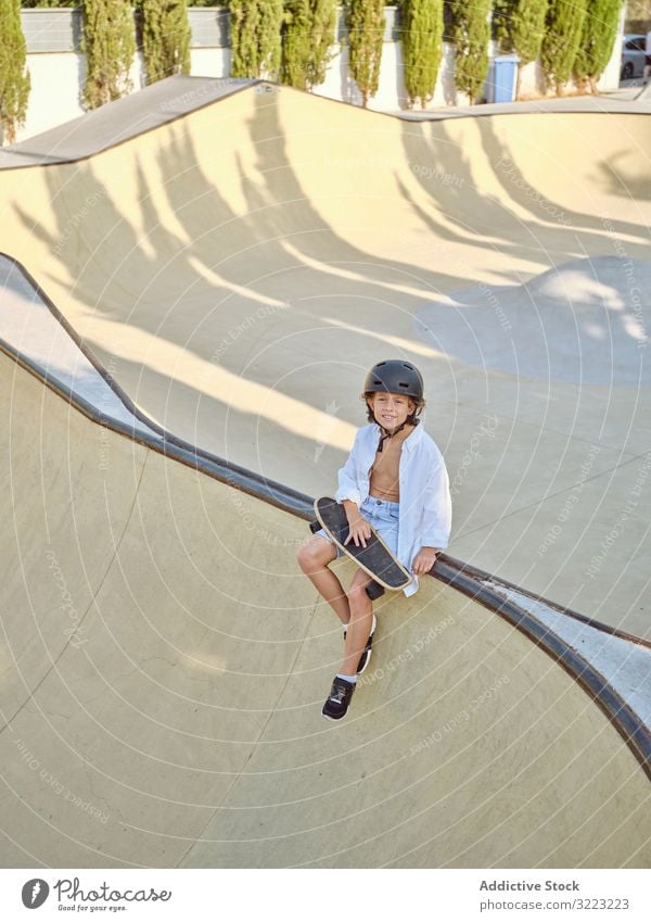 Junge mit Skateboard auf Rampe sitzend Skatepark Schutzhelm Lifestyle Holzplatte Sitzen Sport Freizeit Hobby männlich jung Kindheit Sommer sonnig vorsichtig