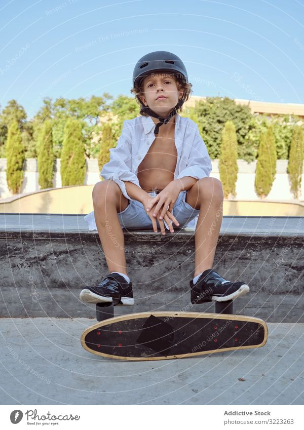 Junge mit Skateboard auf Rampe sitzend Skatepark Schutzhelm Lifestyle Holzplatte Sitzen Sport Freizeit Hobby männlich jung Kindheit Sommer sonnig vorsichtig