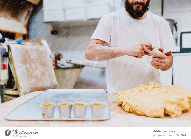 Bärtiger Konditor legt Teig in Tasse Bäckerei Teigwaren setzen Tisch Küche Gebäck Vorbereitung frisch Mann roh professionell Lebensmittel Küchenchef Restaurant