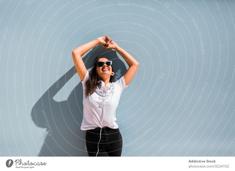 Fröhliche, ungezwungene Frau mit Sonnenbrille steht auf Stadtstraße Kopfhörer stylisch heiter trendy tausendjährig schön Apparatur Musik Gerät stehen Generation