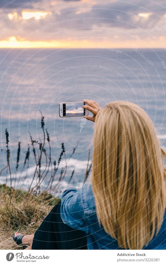 Touristin fotografiert Meer in der Dämmerung Frau Meereslandschaft fotografierend Smartphone Sonnenuntergang Tourismus Horizont Küste malerisch genießen