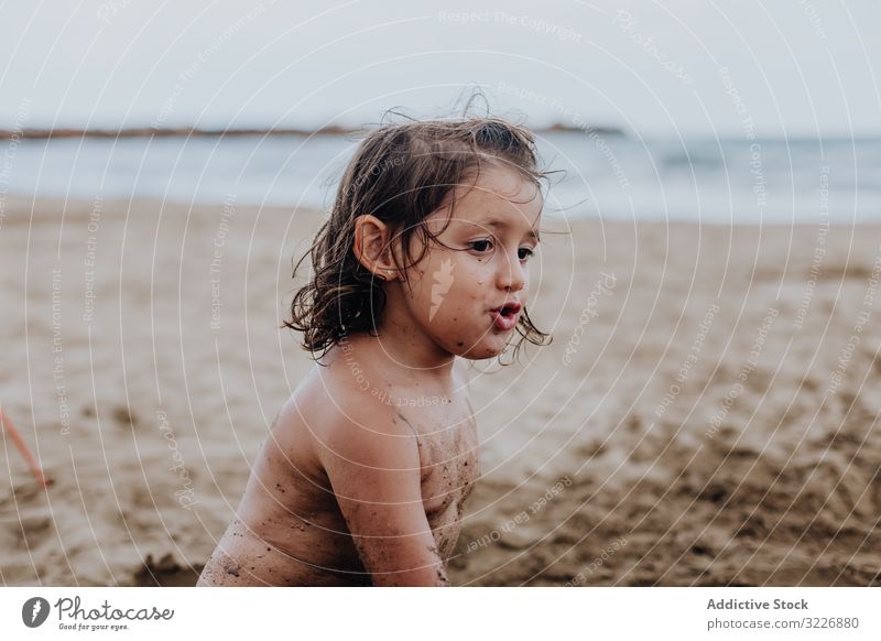 Inspiriertes Kind spielt mit Sand am Strand spielen Sommer Urlaub beschmiert Schürfen Feiertag Spaß Spielen Mund Mädchen Genuss Ausdruck Aktivität heiter