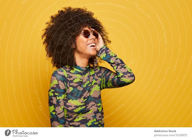 Trendige ethnische Dame mit Sonnenbrille vor hellem Hintergrund Frau farbenfroh cool Afro-Look trendy pulsierend Glück lebhaft Outfit modern Hipster