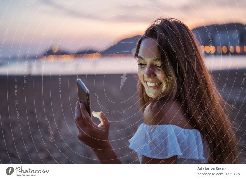 Fröhliche junge Frau benutzt Smartphone im Urlaubsort Strand benutzend soziale Netzwerke Lächeln Resort Abend Sommer Browsen Gerät Apparatur Mobile Telefon