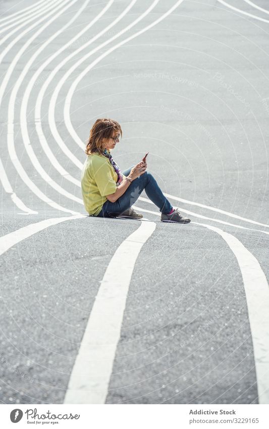 Moderne entspannte Frau auf markierter Straße und Smartphone urban Sitzen Sonnenbrille Erwachsener Asphalt ruhen Weg alternativ sorgenfrei Windstille modern