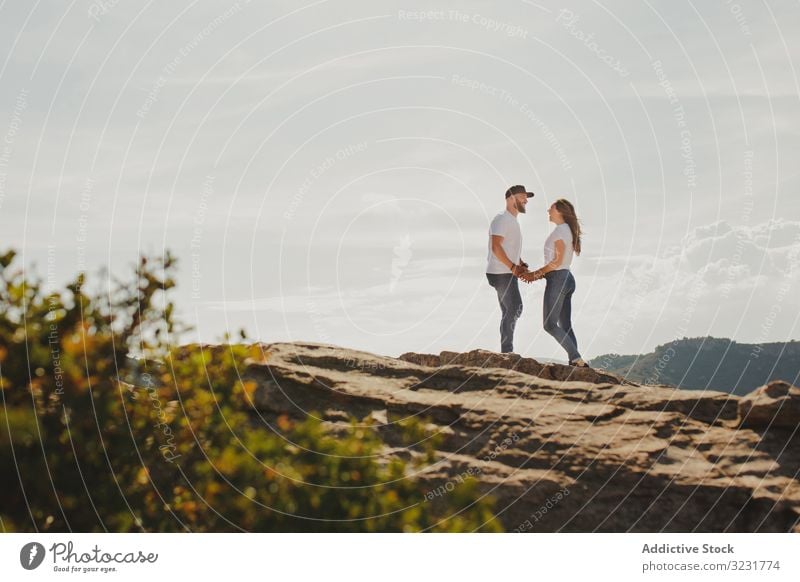 Liebespaar hält Händchen, während es am Bergfelsen steht Paar Berge u. Gebirge Klippe reisen romantisch umarmend stehen Sommer hügelig Berghang heiter modern