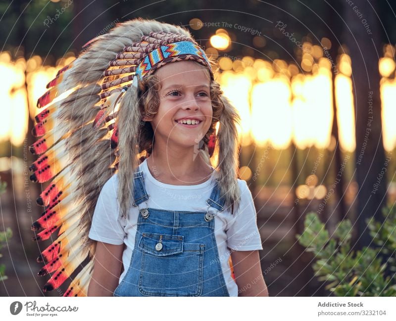 Zufriedenes Kind mit authentischem Hut im Zelt Junge Wigwam Inder Feder Inhalt erfreut Latzhose Jeansstoff Stehen verschränkte Arme Portugal Park Freizeit