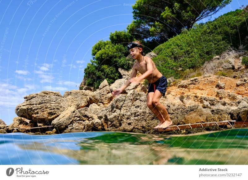 Kleiner Junge macht sich bereit, ins Wasser zu springen MEER Sinkflug Sommer Meeresufer Gleichgewicht Kind Mundschutz Küste reisen aktiv felsig Tourismus Klippe