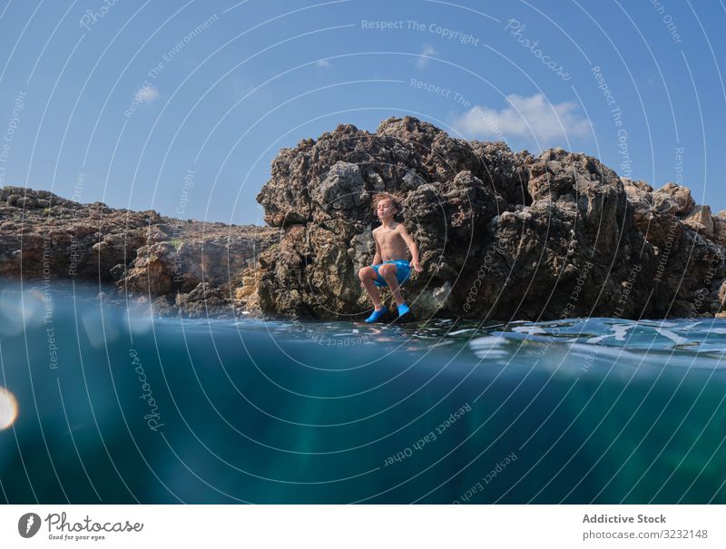 Kleiner Junge springt ins Meer Klippe springen Ufer aktiv Wasser genießen Sommer Himmel sportlich winken Bewegung Kind sonnig aufgeregt Küste Felsen reisen