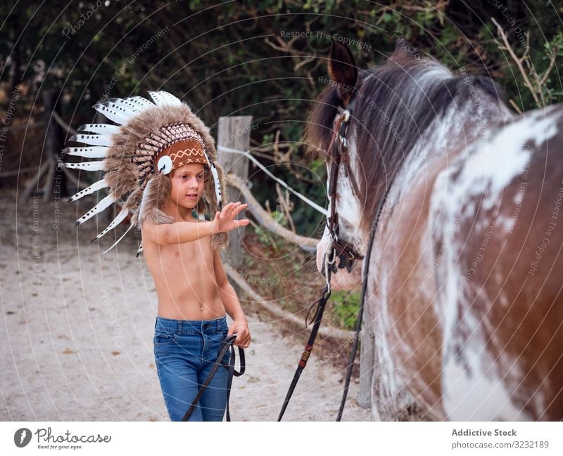 Ruhiger Junge hält Geschirr und geht mit Hengst Pferd Bauernhof Windstille ruhig Cowboy Harmonie Feder Kriegsmütze authentisch Inder Liebe Art Sand ohne Hemd