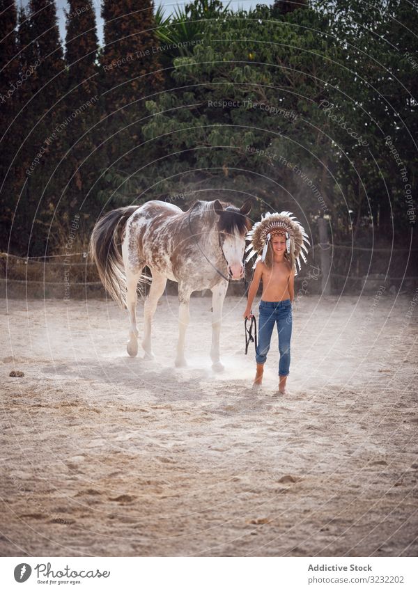 Ruhiger Junge hält Geschirr und geht mit Hengst Pferd Bauernhof Windstille ruhig Cowboy Harmonie Feder Kriegsmütze authentisch Inder Liebe Art Sand ohne Hemd