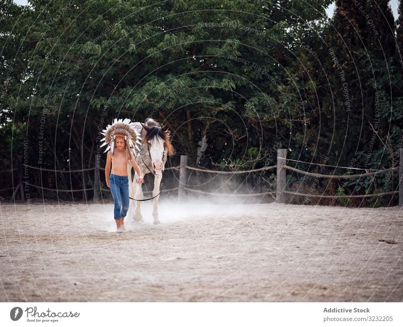 Ruhiger Junge hält Geschirr und geht mit Hengst Pferd Bauernhof Windstille ruhig Cowboy Harmonie Feder Kriegsmütze authentisch Inder Liebe Art Sand ohne Hemd