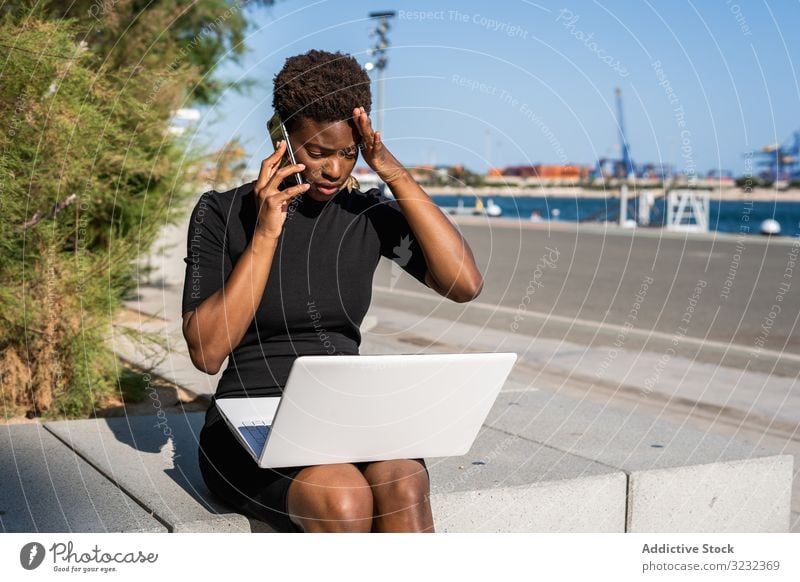 Verzweifelte Frau surft am Laptop und kommuniziert mit dem Handy Smartphone enttäuscht Verzweiflung benutzend Surfen Afroamerikaner Mobile reden Kommunizieren