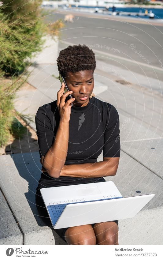 Seriöse Frau surft am Laptop in der Nähe eines modernen Gebäudes sich[Akk] entspannen konzentriert ernst benutzend Surfen Afroamerikaner elegant Straße Kleid