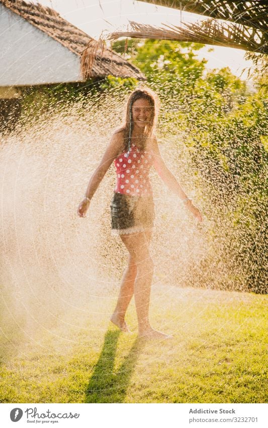 Fröhlicher Teenager hat Spaß mit Wasserstrahl Garten Düsenflugzeug Lachen Sommer Wochenende Mädchen aufgeregt Lifestyle ruhen sich[Akk] entspannen strömen