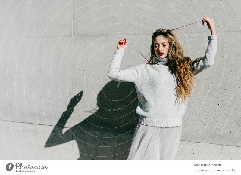 Trendige Dame berührt Haare auf der Straße Frau stylisch sinnlich geschlossene Augen lange Haare elegant Wand Gebäude Model sonnig tagsüber jung cool urban