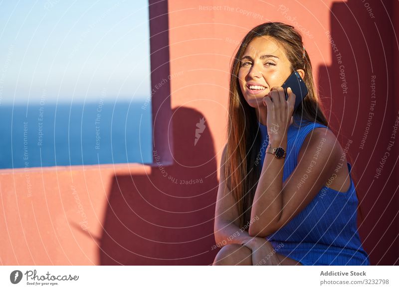 Frau auf einem roten Gebäude mit Smartphone elegant Konstruktion Handy Kleid Sitzen Schritt benutzend Struktur geometrisch Architektur Fassade Wand abstrakt