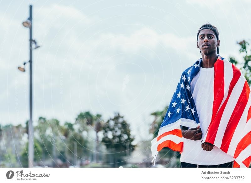 Schwarzer Mann wickelt sich draußen in amerikanische Flagge ein Amerikaner Fahne eingewickelt schwarz Afroamerikaner national Selbstständigkeit aktiv 4. Juli