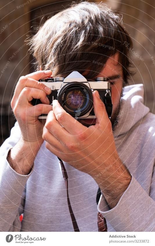 Männlicher Fotograf, der mit einer Kamera auf der Straße fotografiert Fotokamera fotografierend Mann positiv lässig Einstellung benutzend Optik jung Erwachsener