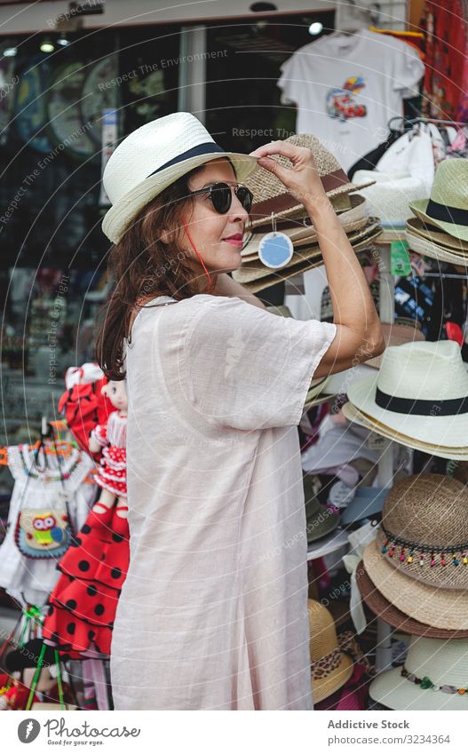 Frau wählt Sommerhut auf Straßenmarkt Strohhut Markt wählen kaufen versuchen Sie passend Accessoire ernst fokussiert selbstbewusst Beschluss u. Urteil