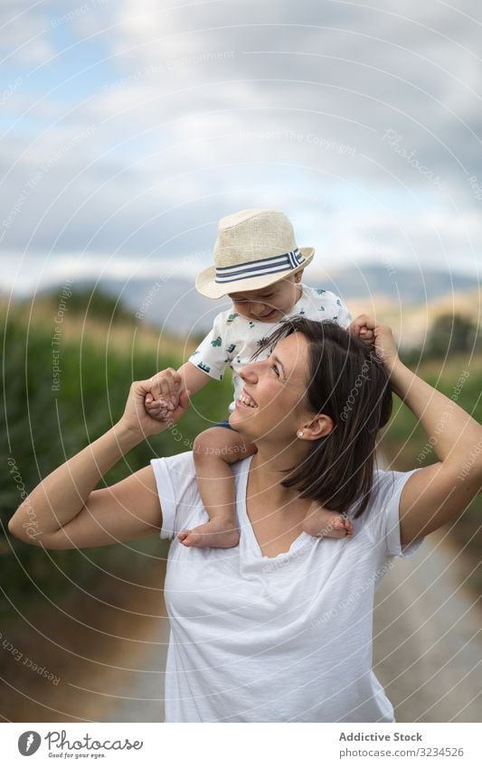 Bezauberndes Kind mit Hut auf den Schultern und die Mutter anschauend Baby Straße Mutterschaft Sommer Pflege lässig Lachen bequem Moment Familie Feld Eltern