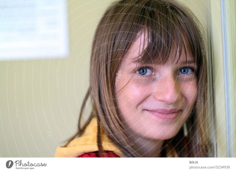 fröhliches, glückliches Mädchen mit Pony und blauen Augen, lehnt an einer Wand von einem Gebäude, und schaut natürlich mit Lächeln in die Kamera. Bildung Schule