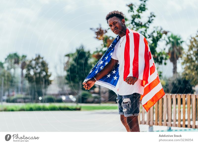 Schwarzer Mann wickelt sich draußen in amerikanische Flagge ein Amerikaner Fahne eingewickelt schwarz Afroamerikaner national Selbstständigkeit aktiv 4. Juli