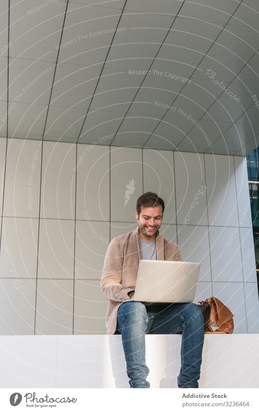 Fröhlicher Geschäftsmann mit Laptop auf der Straße Großstadt benutzend Lächeln sitzen Gebäude Stadtzentrum Business männlich Erwachsener lässig professionell