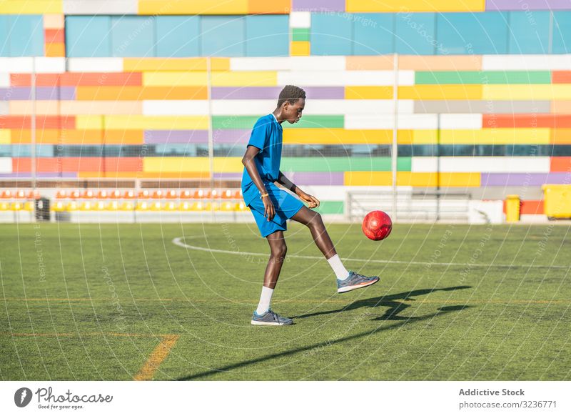 Ethnischer Teenager jongliert mit Fussball Fußball Ball jonglieren Feld Training Spieler Sportbekleidung ethnisch Gras männlich Jugendlicher Knie Rasen sonnig