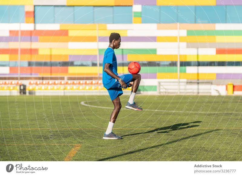 Ethnischer Teenager jongliert mit Fussball Fußball Ball jonglieren Feld Training Spieler Sportbekleidung ethnisch Gras männlich Jugendlicher Knie Rasen sonnig