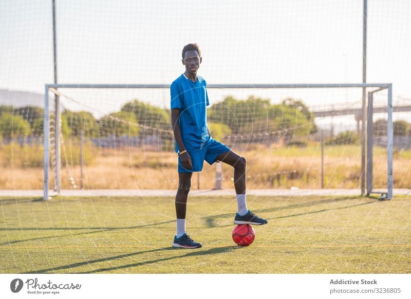 Schwarzer Fussballspieler mit auf dem Stadion stehendem Ball Spieler Fußball Feld Training Sitze Sportbekleidung ethnisch Gras männlich Rasen Netz sonnig