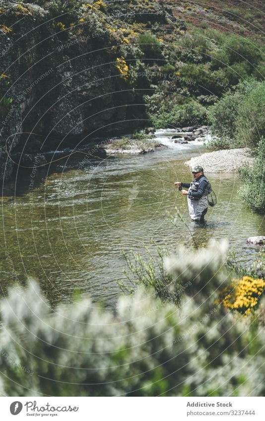 Selbstbewusster Mann fischt mit der Angelrute, während er im Flussstrom steht Fischen strömen selbstbewusst Stab Gerät harling stehen Watvögel Berge u. Gebirge