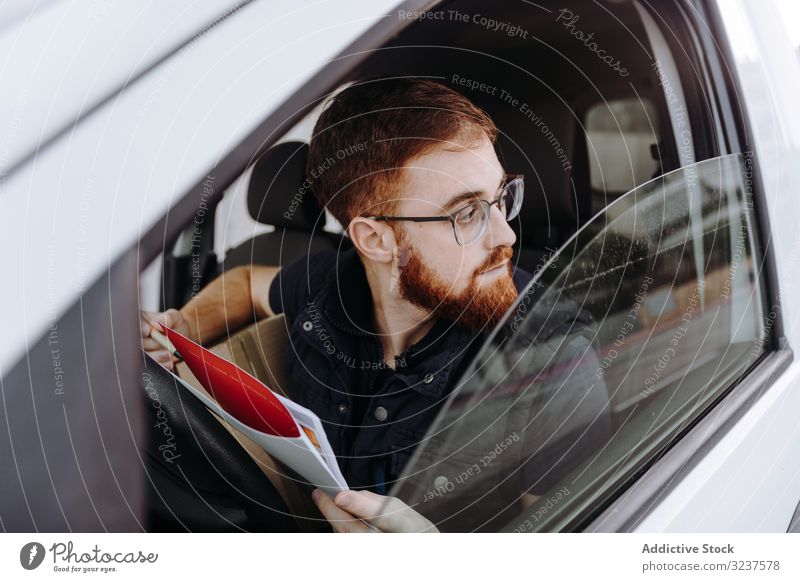 Kurier füllt Papiere aus, während er die Auslieferung der Bestellung an den Kunden im Auto vorbereitet PKW besetzen Versand achtsam Mann schreiben nachdenklich