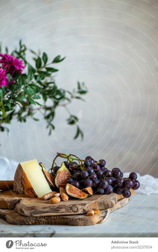 Reife Feigen und dunkelblaue Trauben neben einem Stück Käse auf Schneidebrettern in der Nähe von rosa Blumen frisch Frucht Erfrischung Scheibe Lebensmittel