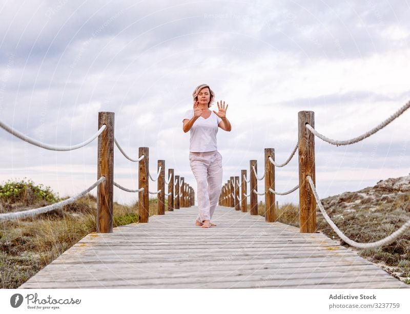 Barfüßige Dame beim Training auf einem Holzweg Frau Atem gestikulieren Übung Weg Tai Chi geschlossene Augen Meditation Natur Himmel wolkig Barfuß Erwachsener