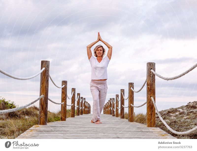 Fröhliche Dame übt auf Holzpfad Frau Atem gestikulieren Übung Weg umklammerte Hände Tai Chi Meditation Natur Himmel wolkig Training Barfuß Erwachsener