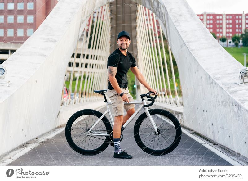 Fröhlicher Mann mit Fahrrad auf Steg stehend Großstadt Mitfahrgelegenheit Brücke modern aktiv sportlich Sommer männlich Erwachsener Glück heiter Lächeln