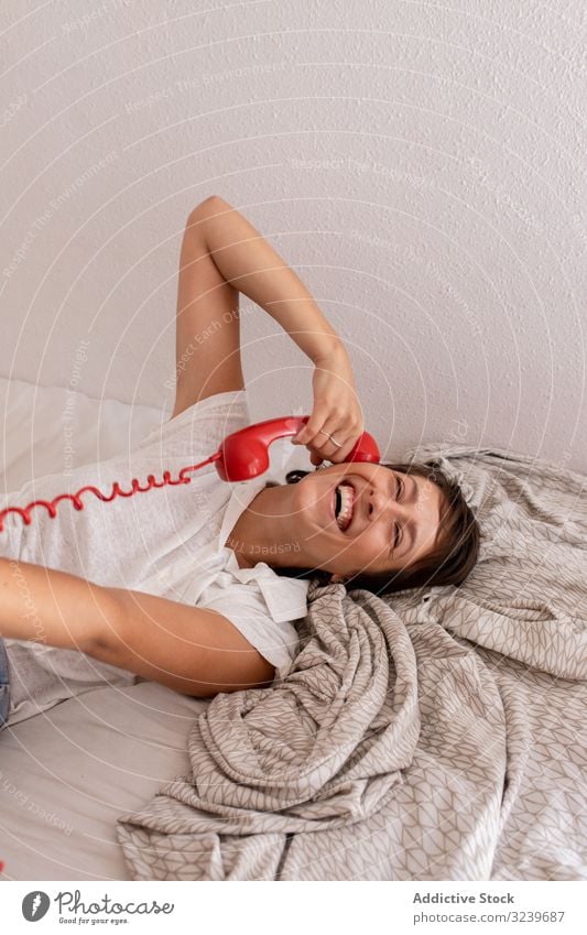 Fröhliche Frau im Telefongespräch Gespräch Lächeln Bett zuhören Dialog Anruf Schlafzimmer Wand heimwärts Appartement flach retro altehrwürdig Mitteilung