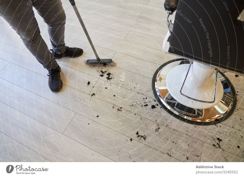 Friseur, der mit dem Besen die Haare eines Kunden fegt, die sich auf dem Holzboden befinden Ausschnitt Salon Kehren Barbershop Business Stock Behaarung