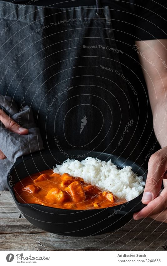 Gesichtsloser Koch hält Bratpfanne mit heißem Butterhähnchen Hähnchen Reis Lebensmittel Speise Inder Küche Curry Basmati lecker Feinschmecker traditionell