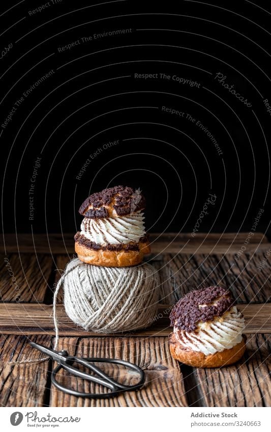 Köstliche Brandteigbrötchen und Wollfäden auf Holztisch choux Sahne Gebäck Dessert Lebensmittel Profiterole Faser Ball Garn Schere selbstgemacht lecker gebacken