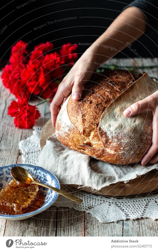 Erntehelfer, der Sauerteigbrot in die Nähe von Blumen und Honig legt Brot Liebling Person Tisch frisch Brotlaib Mahlzeit Lebensmittel Wabe gebacken rustikal